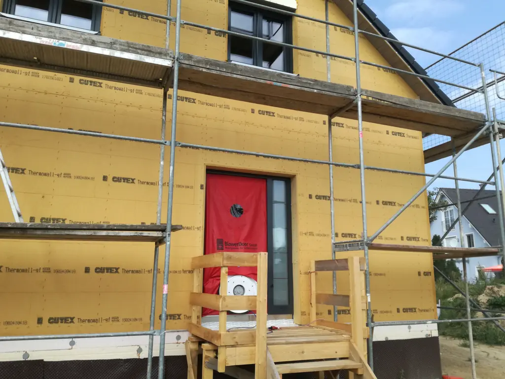 Neubau in Holzrahmenbauweise mit gelber Holzfaser-Dämmplatte an der Fassade und Gerüst