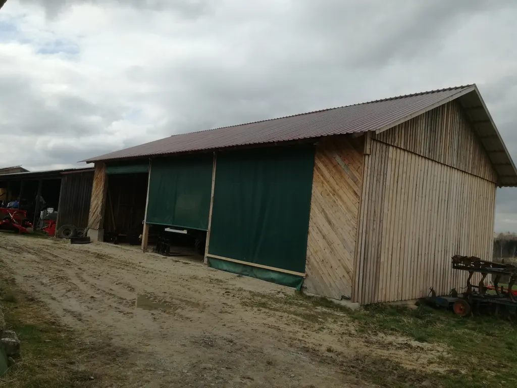 Landwirtschaftliche Halle in Holzbauweise mit Pultdach, Holzverschalung und grünen Planen