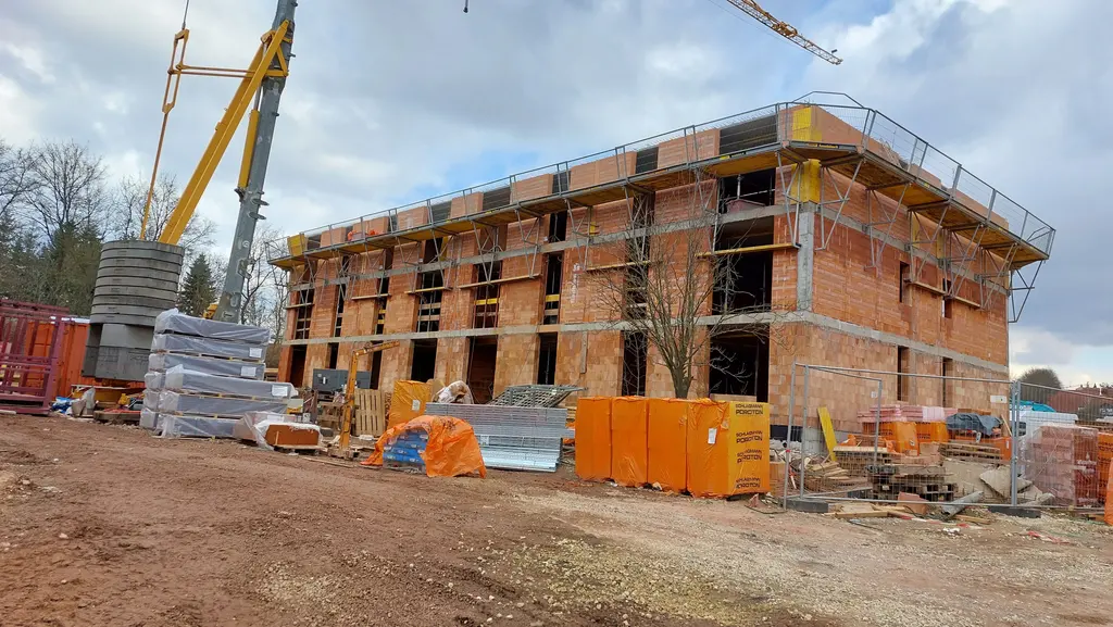 Mehrgeschossiger Mehrfamilienhaus-Neubau im Ziegelrohbau mit Kran und Baustoffen auf der Baustelle